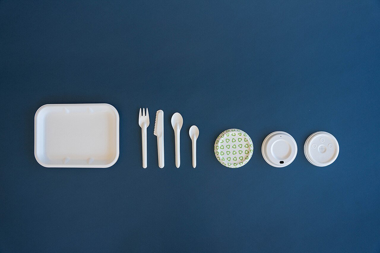 White container, utensils and cup lids arranged on a blue background